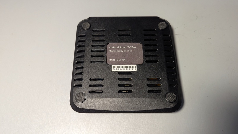 The bottom of the Keuby Ice 0515. There are vent holes all over. A gray tag says, "Android Smart TV Box, Model: Keuby Ice 0515, MADE IN CHINA". A smaller white tag lists its MAC address and a barcode.